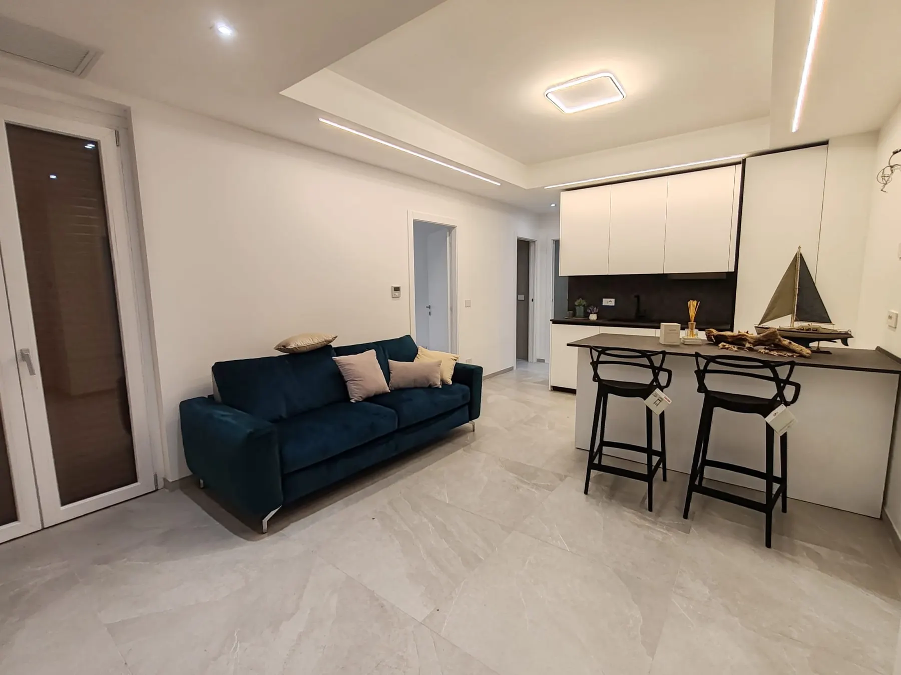 Soggiorno con divano blu e cucina con penisola dell'appartamento ristrutturato ad Alassio